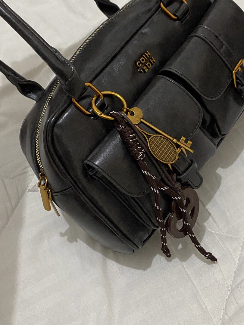 Black Handbag dual pocket (Category: Luxury Bags & Wallets) located in Aliaga. Submitted by dudarling (Listing ID 1436869464, Image 3). Description: - Black handbag - Gold-colored hardware - Two front pockets - Top zipper closure - Two top handles - Decorative tennis racket keychain - Rectangular shape - Glossy material - Black interior.