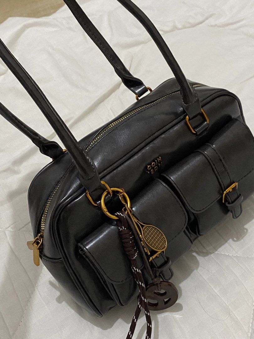 Black Handbag dual pocket (Category: Luxury Bags & Wallets) located in Aliaga. Submitted by dudarling (Listing ID 1436869464, Image 2). Description: - Black handbag - Gold-colored hardware - Two front pockets - Top zipper closure - Two top handles - Decorative tennis racket keychain - Rectangular shape - Glossy material - Black interior.