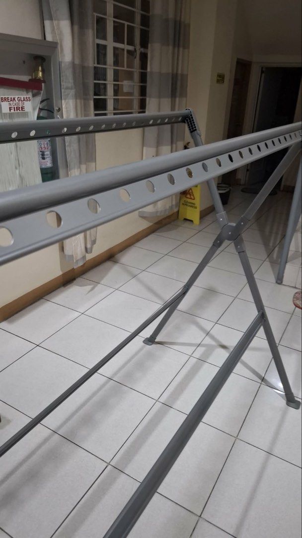 Foldable Clothes Drying Rack (Category: Clothes Drying Rack) located in Manila. Submitted by ccbeltran (Listing ID 1436945198, Image 3). Description: - Foldable clothes drying rack - Suitable for indoor and outdoor use - Features multiple bars for hanging clothes - Sturdy, X-shaped base for stability - Made of metal with a gray finish - Folds up easily for storage - Great for apartments and limited spaces.