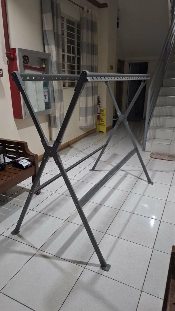 Foldable Clothes Drying Rack (Category: Clothes Drying Rack) located in Manila. Submitted by ccbeltran (Listing ID 1436945198, Image 1). Description: - Foldable clothes drying rack - Suitable for indoor and outdoor use - Features multiple bars for hanging clothes - Sturdy, X-shaped base for stability - Made of metal with a gray finish - Folds up easily for storage - Great for apartments and limited spaces.