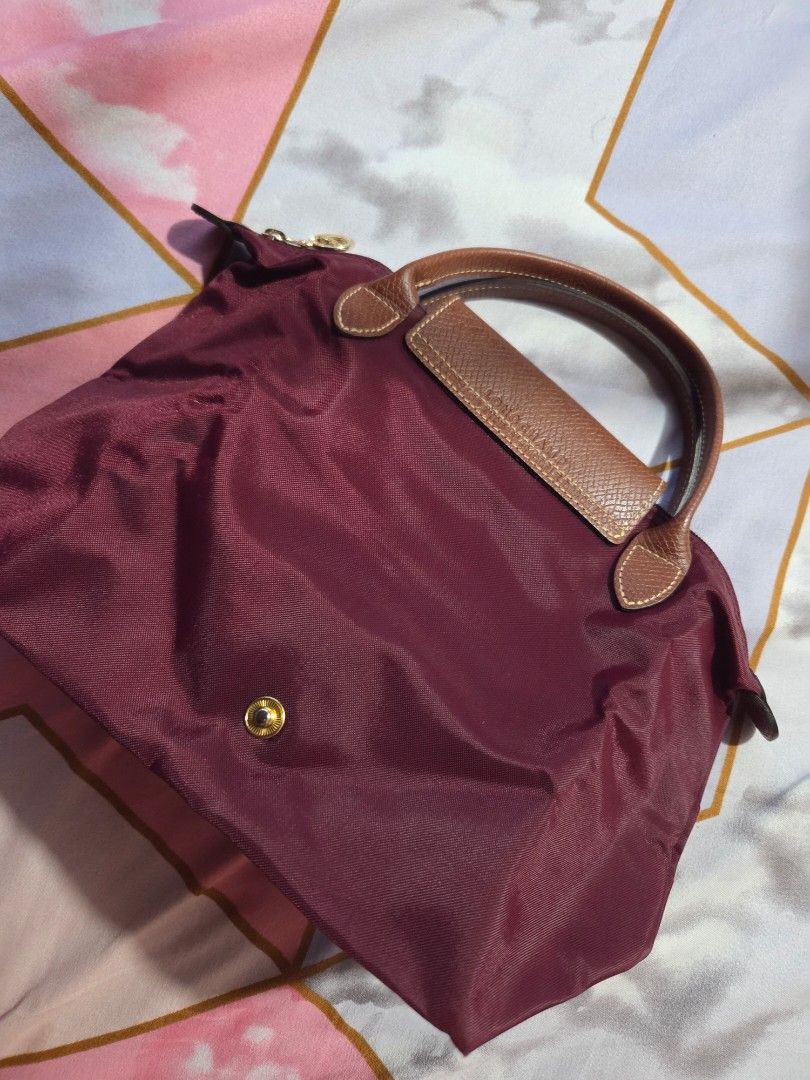 Longchamp Le Pliage Handbag - Burgundy (Category: Luxury Bags & Wallets) located in Makati City. Submitted by ellabit4379213 (Listing ID 1436921503, Image 1). Description: - Authentic Longchamp Le Pliage handbag - Color: Burgundy - Features brown leather handles and flap - Gold-tone button closure - Rectangular shape when folded - Made of a nylon-like material - Rounded, stitched handles - Simple, classic design.