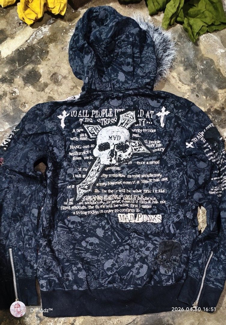 Mad Punks Skull Print Hooded Jacket (Category: Coats, Jackets and Outerwear) located in Baguio. Submitted by caid0 (Listing ID 1436876095, Image 2). Description: Black hooded jacket with a skull print design. Features a faux fur-lined hood and a zip-up closure. Embellished with patches that read "Mad Punks". The jacket has a ribbed hem and cuffs. The design includes various skull graphics and text details. A red tag is visible on the right side..