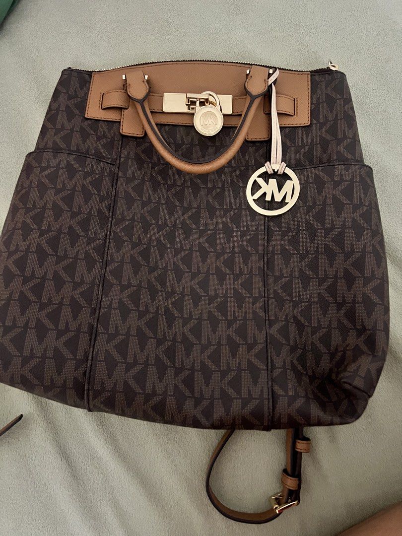 Michael Kors Backpack Handbag (Category: Luxury Bags & Wallets) located in Calamba. Submitted by ilhianacol29753 (Listing ID 1436829571, Image 1). Description: - Authentic Michael Kors backpack handbag - Brown MK logo print - Top handle and adjustable straps - Multiple interior pockets - Gold-tone lock closure - Metal MK logo charm - Michael Kors logo interior lining - Brown and tan color scheme.