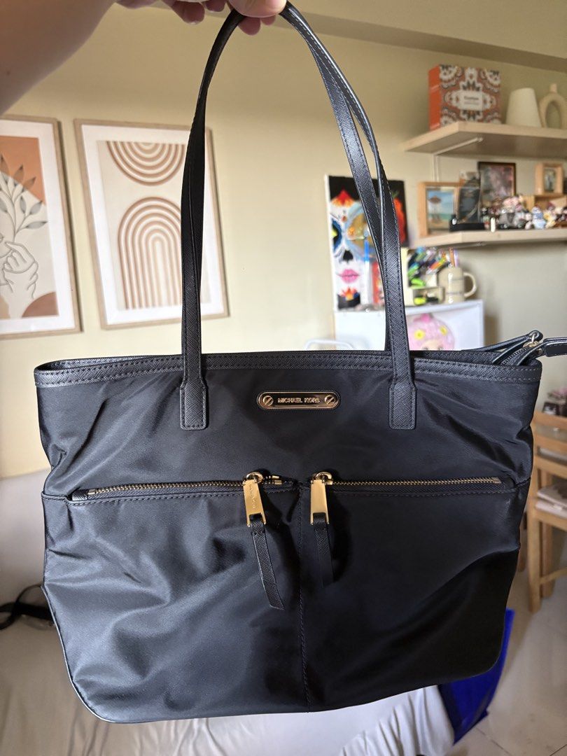 Michael Kors Nylon Black Tote Bag (Category: Tote Bags) located in Pasay City. Submitted by laann00 (Listing ID 1437017327, Image 3). Description: Lightly used Black Michael Kors tote bag with gold-toned hardware. Features two front zipper pockets and a spacious interior with the Michael Kors logo lining. Includes two top handles for carrying. Minor flaw shown in pic ( 1 handle). RFS decluttering..