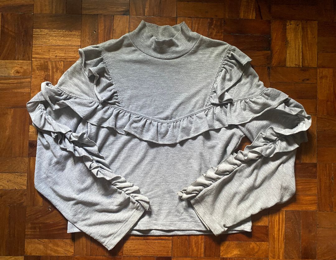 Pre-Loved H&M Gray Ruffle Long Sleeve Blouse (Category: Blouses) located in Mandaluyong City. Submitted by bontiques (Listing ID 1436842054, Image 1). Description: ITEM DESCRIPTION ⭐️ Light gray mock neck blouse ⭐️ Long sleeves with ruffle detailing ⭐️ Lightly fitted silhouette ⭐️ Stretchy fabric ⭐️ Shoulder to Hem: 21 inches ⭐️ Chest: 18 inches ⭐️ Measurements in photos DELIVERY & PAYMENT ⭐️ Gcash QR ⭐️ Lalamove (within 1-2 days or ASAP) ⭐️ J&T 