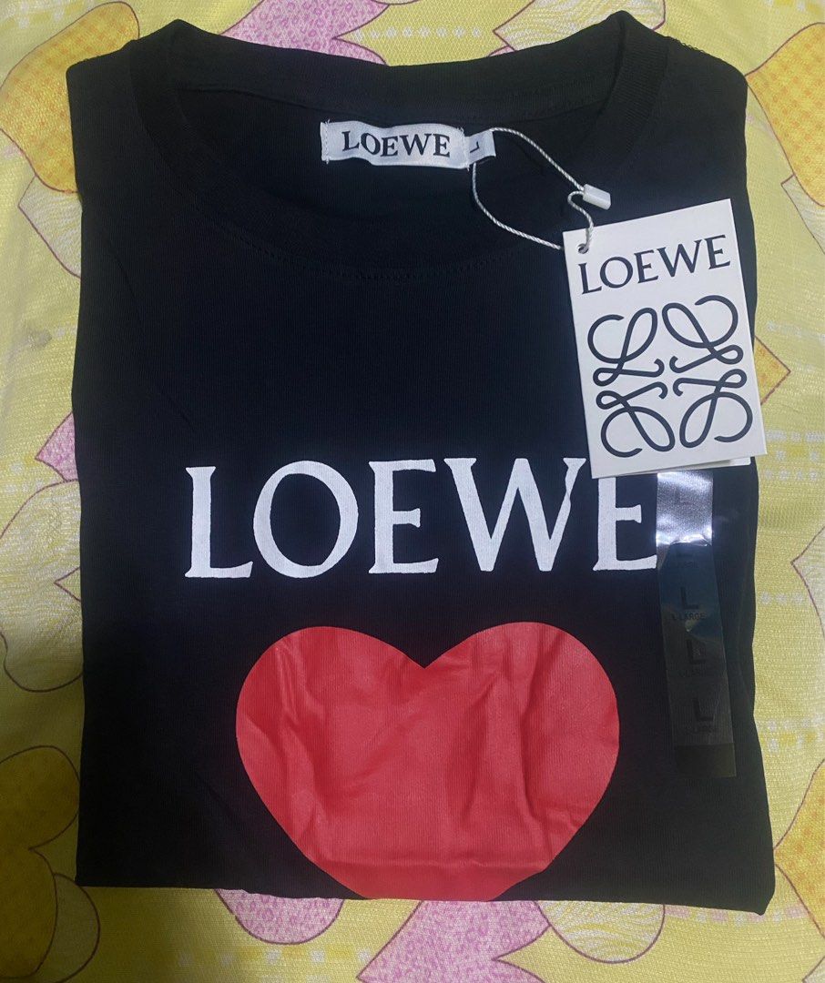 Loewe Heart Logo T-shirt (Category: Shirts) located in Cavite. Submitted by Abril_07 (Listing ID 1431536443, Image 2). Description: - Loewe black t-shirt - Features a red heart graphic and Loewe logo - Crew neck and short sleeves - Unworn condition - Original tag attached - Size clearly indicated on tag - Classic and stylish design.