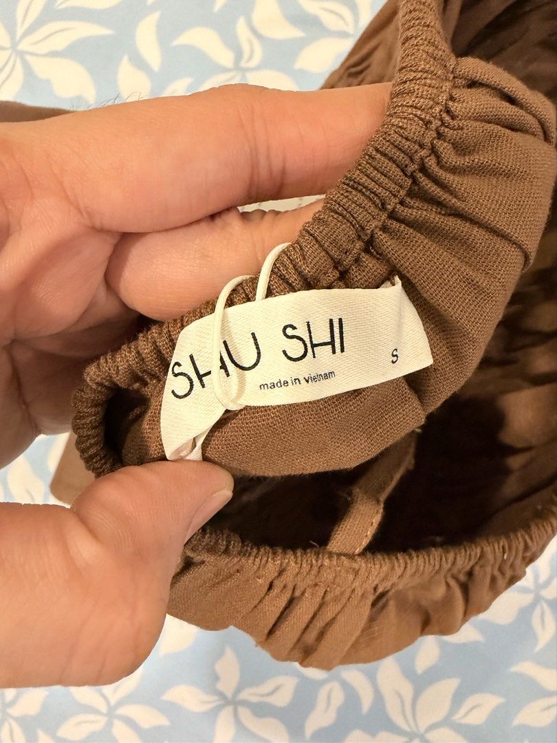 SHU SHI Brown Strap Top Linen Muse Top (Category: Sleeveless) located in Imus. Submitted by yummyfinds (Listing ID 1441302929, Image 3). Description: - Cute brown smocked top from SHU SHI - Features a tie front detail - Flattering peplum hem - Adjustable spaghetti straps - Made in Vietnam - Versatile: pairs well with white linen pants or jeans - Ideal for casual days or beach vacations.