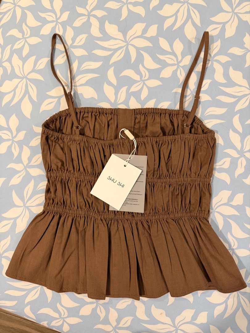 SHU SHI Brown Strap Top Linen Muse Top (Category: Sleeveless) located in Imus. Submitted by yummyfinds (Listing ID 1441302929, Image 2). Description: - Cute brown smocked top from SHU SHI - Features a tie front detail - Flattering peplum hem - Adjustable spaghetti straps - Made in Vietnam - Versatile: pairs well with white linen pants or jeans - Ideal for casual days or beach vacations.