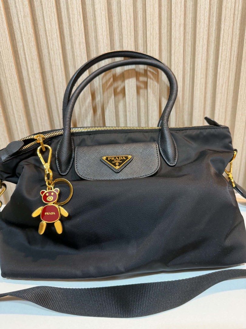 Prada Nylon Tote Bag with Bear Charm (Category: Luxury Bags & Wallets) located in Quezon City. Submitted by kymis (Listing ID 1443119584, Image 1). Description: - Authentic Black Prada Nylon Tote Bag - Features a cute teddy bear charm - Genuine leather trim and handles - Elegant gold-tone hardware - Comes with a detachable shoulder strap - Ideal for everyday use -Coating along the handle has cracked, peeled a little.