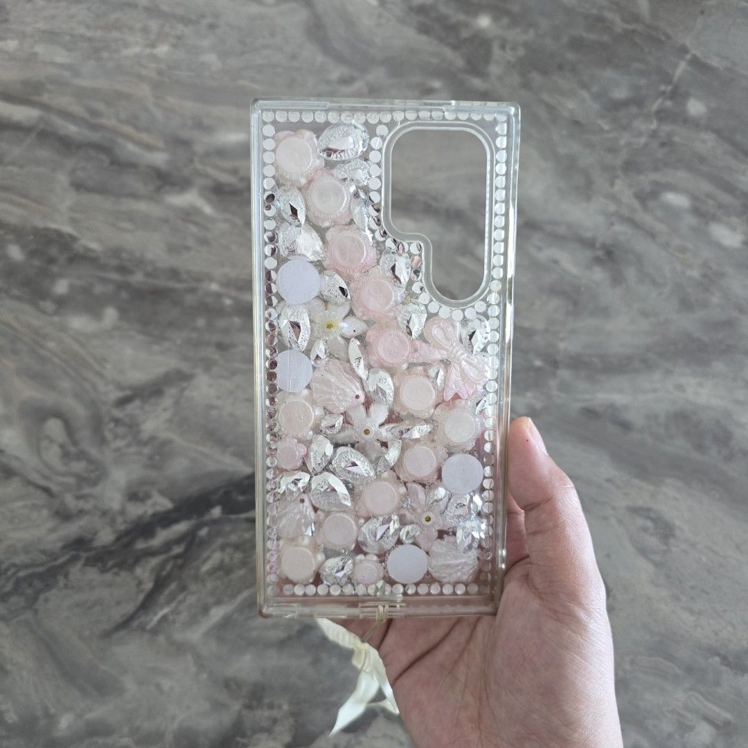 S24 Ultra Custom Bling Phone Case with Charm (Category: Cases & Sleeves) located in Mandaluyong City. Submitted by _monamourph (Listing ID 1442950164, Image 3). Description: - Super cute phone case adorned with dazzling rhinestones and charming 3D flowers. - Includes a matching pearl and bow charm strap for added flair. - Handmade and one-of-a-kind design. - Provides stylish protection for your phone. Bought for 450 in GH. Slightly used onlu sell