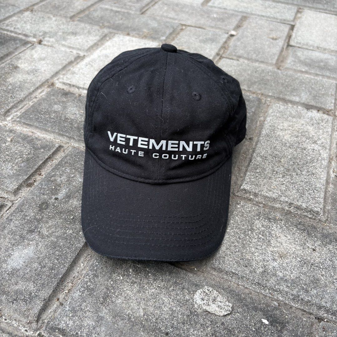Vetements Haute Couture Reflective Cap (Category: Caps & Hats) located in Naga. Submitted by reshelled (Listing ID 1443027527, Image 1). Description: Condition: Pre-owned, good condition. Minor signs of wear (light fading on the fabric, consistent with normal use). Description: Iconic black dad cap from Vetements. Features bold white reflective “VETEMENTS HAUTE COUTURE” lettering across the front. This minimalist yet statement-making piece is a s