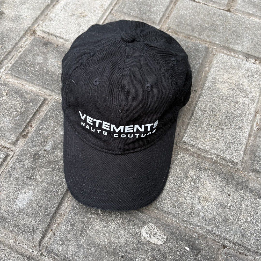 Vetements Haute Couture Reflective Cap (Category: Caps & Hats) located in Naga. Submitted by reshelled (Listing ID 1443027527, Image 2). Description: Condition: Pre-owned, good condition. Minor signs of wear (light fading on the fabric, consistent with normal use). Description: Iconic black dad cap from Vetements. Features bold white reflective “VETEMENTS HAUTE COUTURE” lettering across the front. This minimalist yet statement-making piece is a s