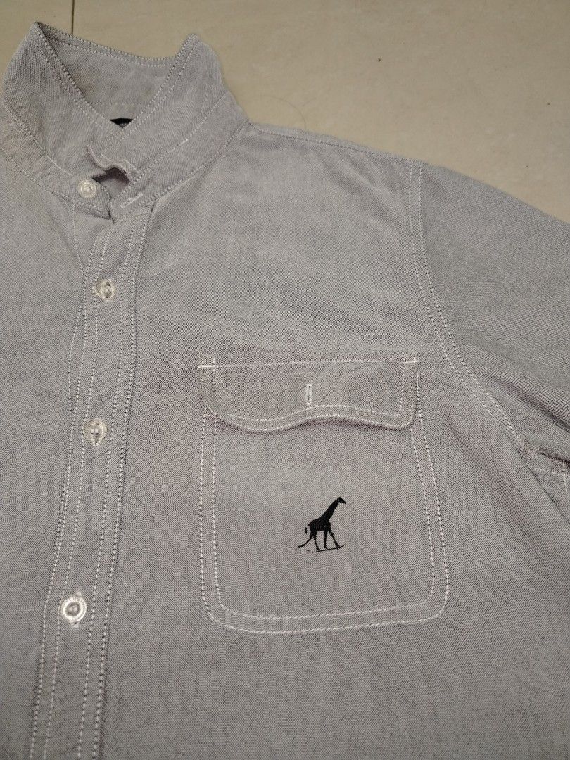 Gray Short Sleeve Button Up Shirt with Giraffe Logo (Category: Tshirts & Polo Shirts ) located in San Pablo. Submitted by nhatzstuffz (Listing ID 1443275270, Image 2). Description: - Gray short sleeve button-up shirt - Size M - Two chest pockets - Small embroidered giraffe logo on left pocket - Button-down collar - Casual everyday style - Ideal for warm weather.