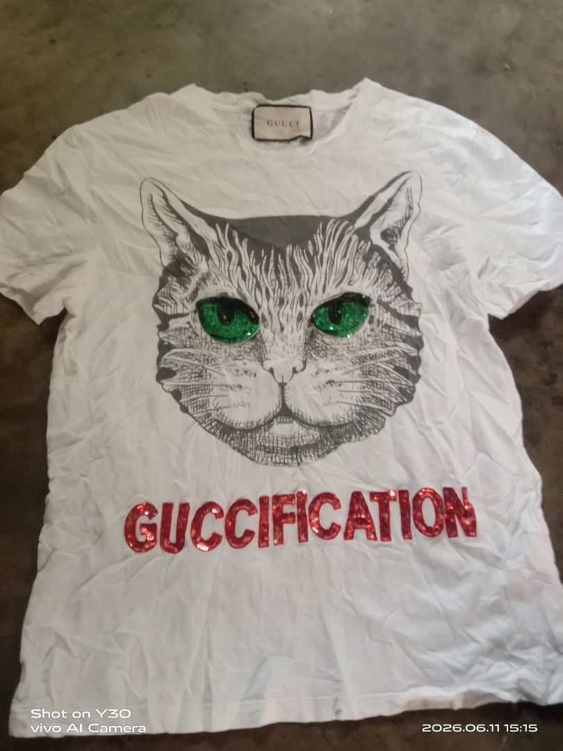 Gucci White Cat "GUCCIFICATION" Sequin T-Shirt (Category: Luxury Apparel) located in Cabuyao City. Submitted by blake657 (Listing ID 1443194527, Image 1). Description: - Authentic white Gucci T-shirt - Features a cool cat graphic - Cat's eyes are sparkling green sequins - "GUCCIFICATION" text in vibrant red sequins - Genuine Gucci tag - Perfect statement piece to elevate your style.