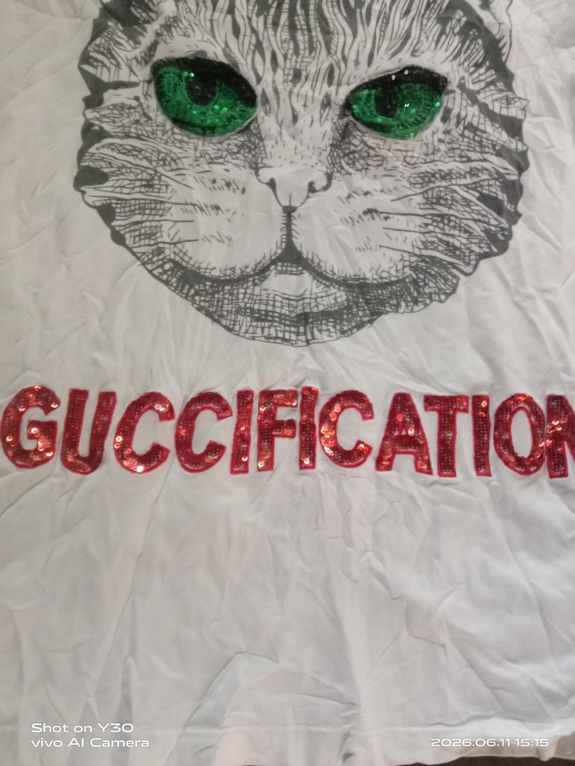 Gucci White Cat "GUCCIFICATION" Sequin T-Shirt (Category: Luxury Apparel) located in Cabuyao City. Submitted by blake657 (Listing ID 1443194527, Image 2). Description: - Authentic white Gucci T-shirt - Features a cool cat graphic - Cat's eyes are sparkling green sequins - "GUCCIFICATION" text in vibrant red sequins - Genuine Gucci tag - Perfect statement piece to elevate your style.