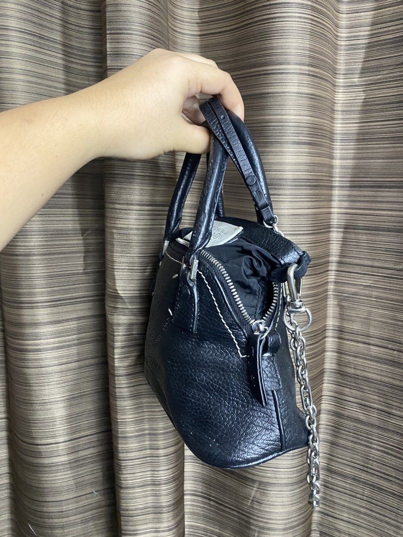Maison Margiela Black Leather 5AC Mini Bag (Category: Luxury Bags & Wallets) located in Tacloban City. Submitted by houseofluxury.co (Listing ID 1443250367, Image 2). Description: - Sleek black leather mini bag - Versatile top handle and silver chain strap - Secure zipper closure - Protective studded base - Signature white stitching detail on the front - Compact size, ideal for carrying essentials.