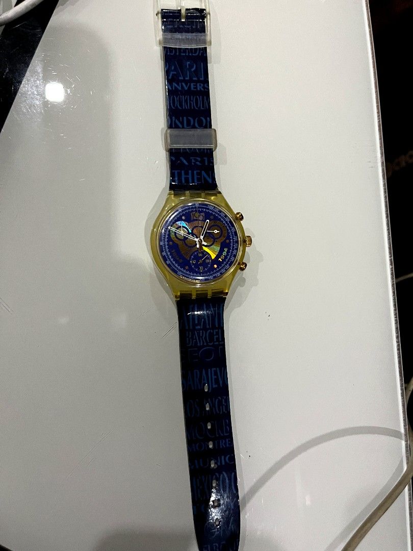 Vintage Swatch Olympic Games Chronograph Watch (Category: Men's Watches) located in Naga. Submitted by kenshin78 (Listing ID 1443246155, Image 3). Description: - Swatch Watch from the Olympic Games Collection - Year: 1994 - Dial: Blue with city names and '1994' details - Strap: Features 'Remember Sarajevo' and Olympic rings - Case: Gold-tone with chronograph pushers - Unique collector's item for sports enthusiasts.