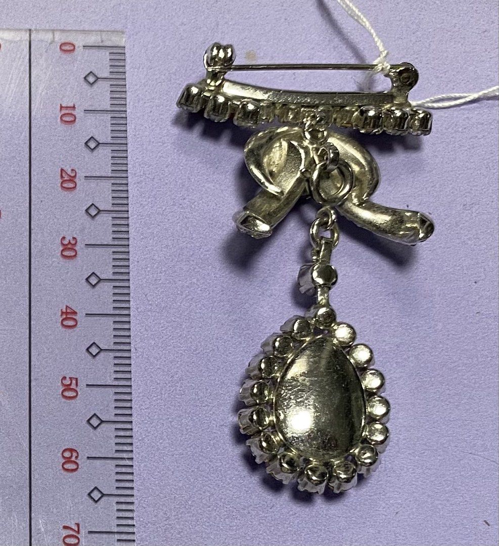 Vintage Rhinestone Bow Brooch with Red Pear Drop (Category: Brooches) located in Mabalacat. Submitted by somethingoldsomethingnew28 (Listing ID 1443190551, Image 2). Description: - Vintage bow brooch, detachable pendant - Adorned with clear rhinestones - Features a dangling red pear-shaped stone - Secure pin closure on the back - Approximately 7cm in length - Adds a touch of sparkle and elegance to any outfit.