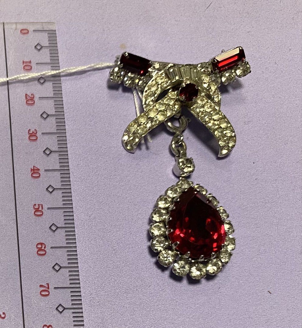 Vintage Rhinestone Bow Brooch with Red Pear Drop (Category: Brooches) located in Mabalacat. Submitted by somethingoldsomethingnew28 (Listing ID 1443190551, Image 1). Description: - Vintage bow brooch, detachable pendant - Adorned with clear rhinestones - Features a dangling red pear-shaped stone - Secure pin closure on the back - Approximately 7cm in length - Adds a touch of sparkle and elegance to any outfit.