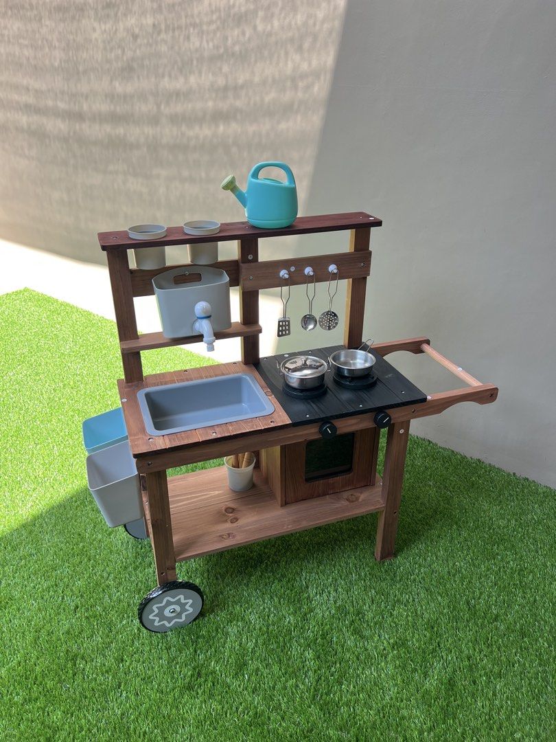Wooden Mud Kitchen Playset with Accessories (Category: Kids Toys) located in Mandaluyong City. Submitted by timberthinksph (Listing ID 1443271658, Image 3). Description: - Sturdy wooden mud kitchen for kids - Includes sink, stovetop, and oven - Comes with hanging utensils, pots, watering can, and gardening tools - Ideal for outdoor imaginative play - Features wheels for easy portability.