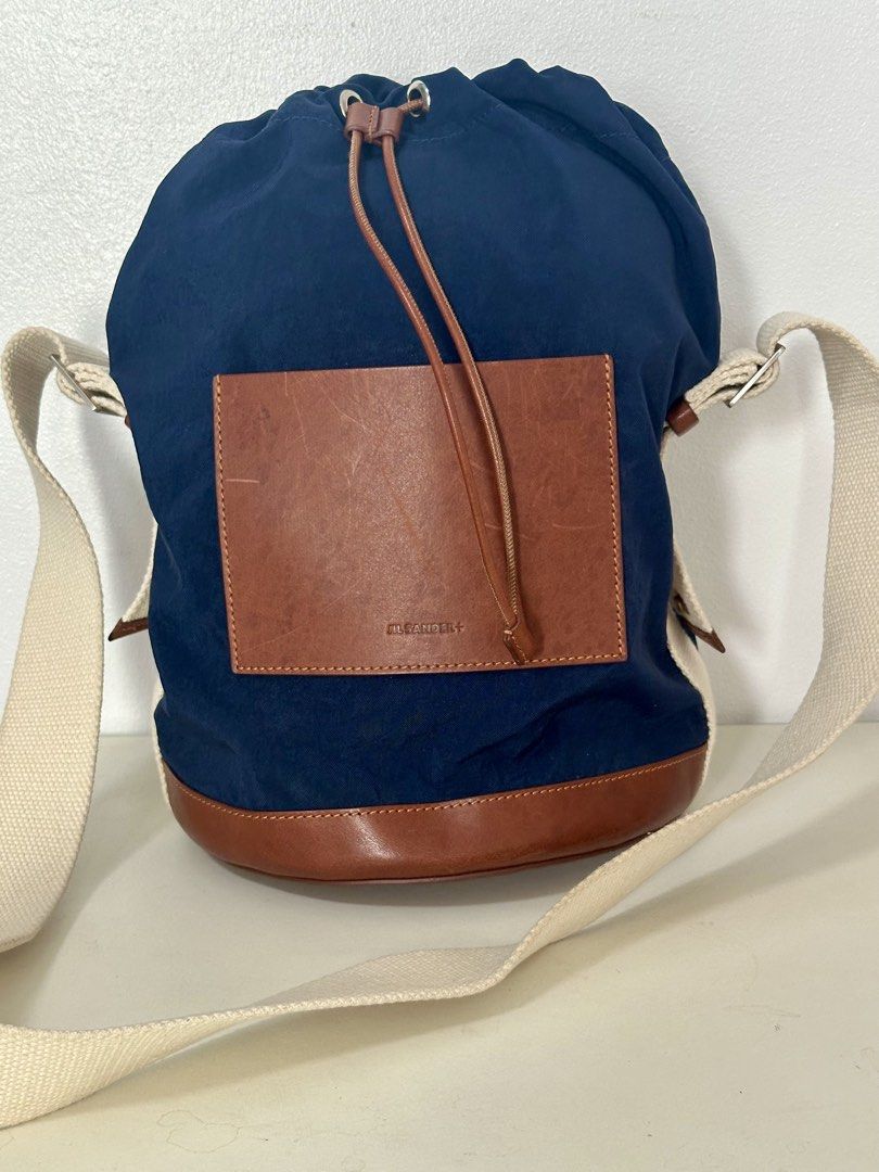 Jil Sander+ Navy Blue Canvas Leather Trim Drawstring Bag (Category: Luxury Bags & Wallets) located in Mandaluyong City. Submitted by mabv85 (Listing ID 1443370619, Image 2). Description: - Authentic Jil Sander navy blue canvas drawstring bag - Brown leather trim and pocket - Adjustable strap for crossbody or shoulder wear - Made in Italy - Includes original tag.