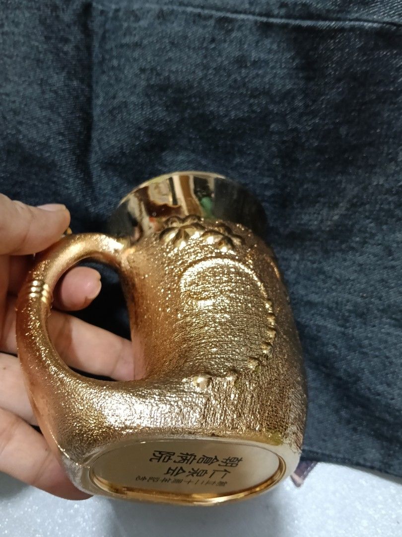 Gold Embossed Floral Mug with Unique Handle (Category: Coffee & Tea Tableware) located in Caloocan City. Submitted by jeenbeebiz (Listing ID 1443652289, Image 3). Description: - Stunning gold mug with detailed floral embossing. - Unique textured body for a comfortable grip. - Features a stylish, curved handle. - Smooth and shiny interior for easy cleaning. - Includes intriguing Chinese characters on the bottom. - Perfect as a decorative display p