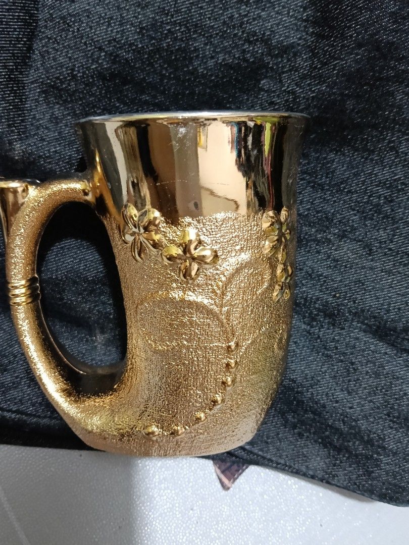 Gold Embossed Floral Mug with Unique Handle (Category: Coffee & Tea Tableware) located in Caloocan City. Submitted by jeenbeebiz (Listing ID 1443652289, Image 1). Description: - Stunning gold mug with detailed floral embossing. - Unique textured body for a comfortable grip. - Features a stylish, curved handle. - Smooth and shiny interior for easy cleaning. - Includes intriguing Chinese characters on the bottom. - Perfect as a decorative display p