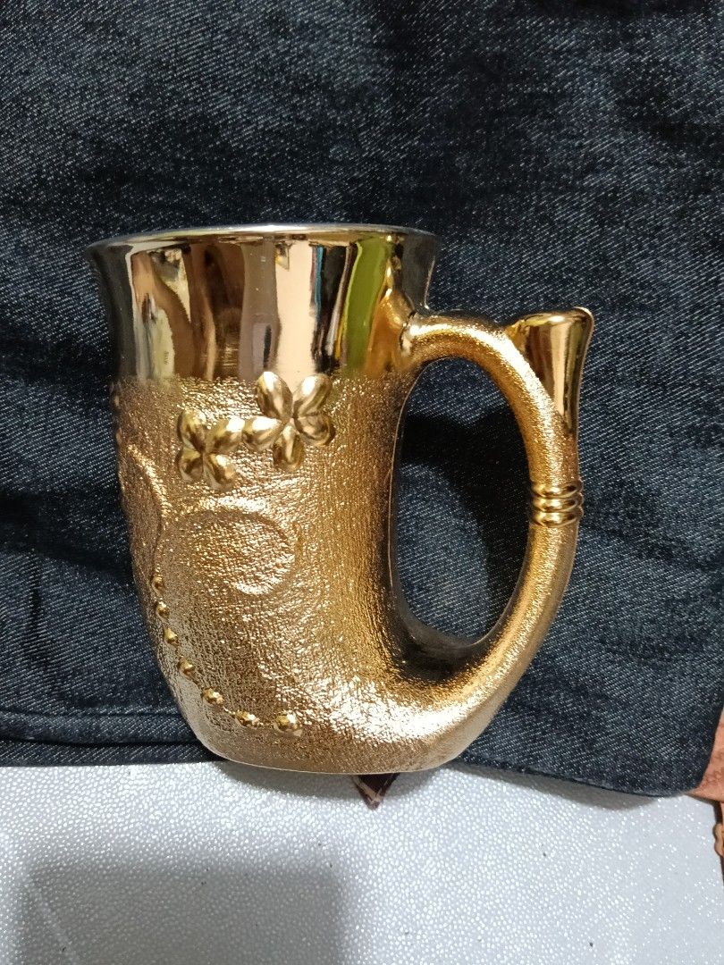 Gold Embossed Floral Mug with Unique Handle (Category: Coffee & Tea Tableware) located in Caloocan City. Submitted by jeenbeebiz (Listing ID 1443652289, Image 2). Description: - Stunning gold mug with detailed floral embossing. - Unique textured body for a comfortable grip. - Features a stylish, curved handle. - Smooth and shiny interior for easy cleaning. - Includes intriguing Chinese characters on the bottom. - Perfect as a decorative display p
