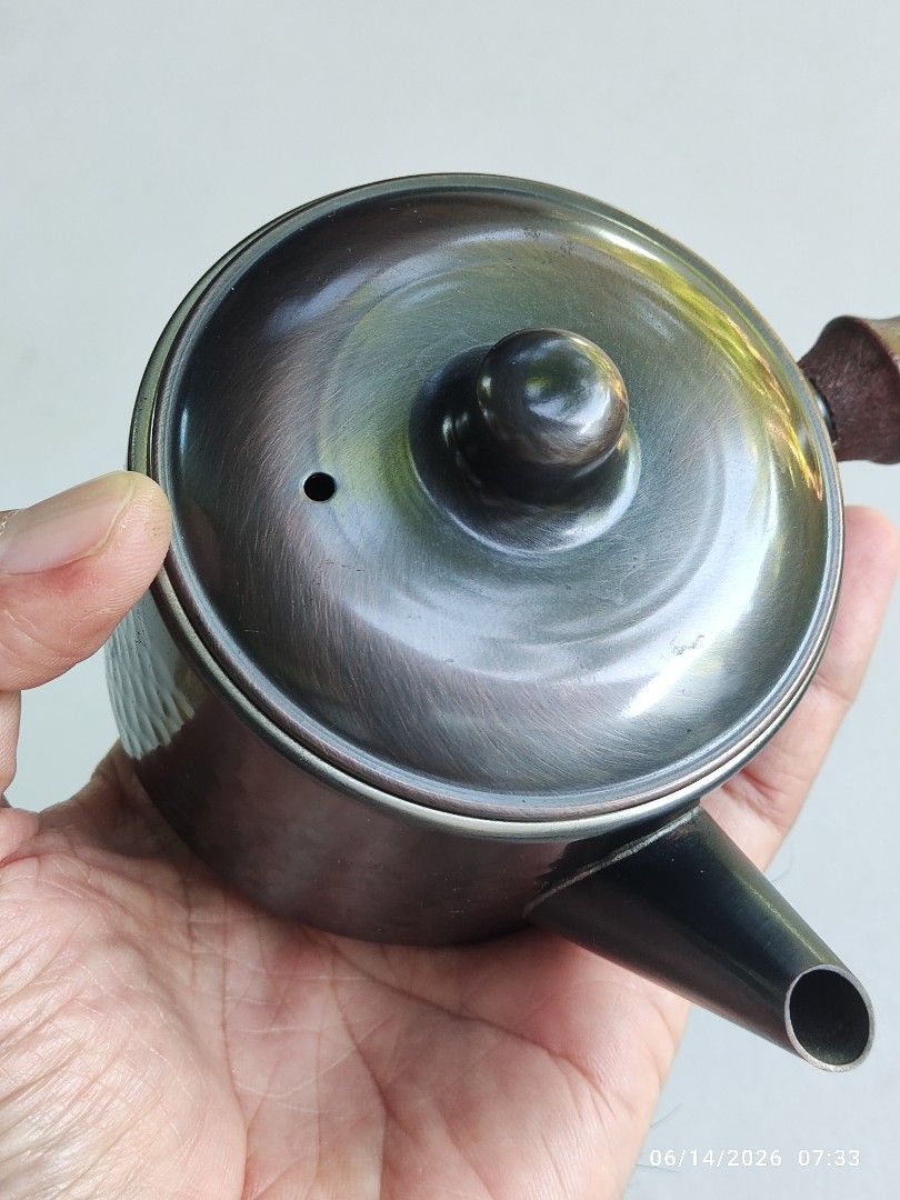 Hammered Copper Teapot with Wooden Handle (Category: Coffee & Tea Tableware) located in Tagum. Submitted by cs1907 (Listing ID 1443701207, Image 3). Description: - Small teapot with a unique hammered metal exterior. - Features a comfortable dark wooden handle. - Snugly fitting lid ensures a good pour. - Versatile: perfect for serving tea or as a charming decorative piece. - Great addition to a small kitchen or any tea lover's collection..