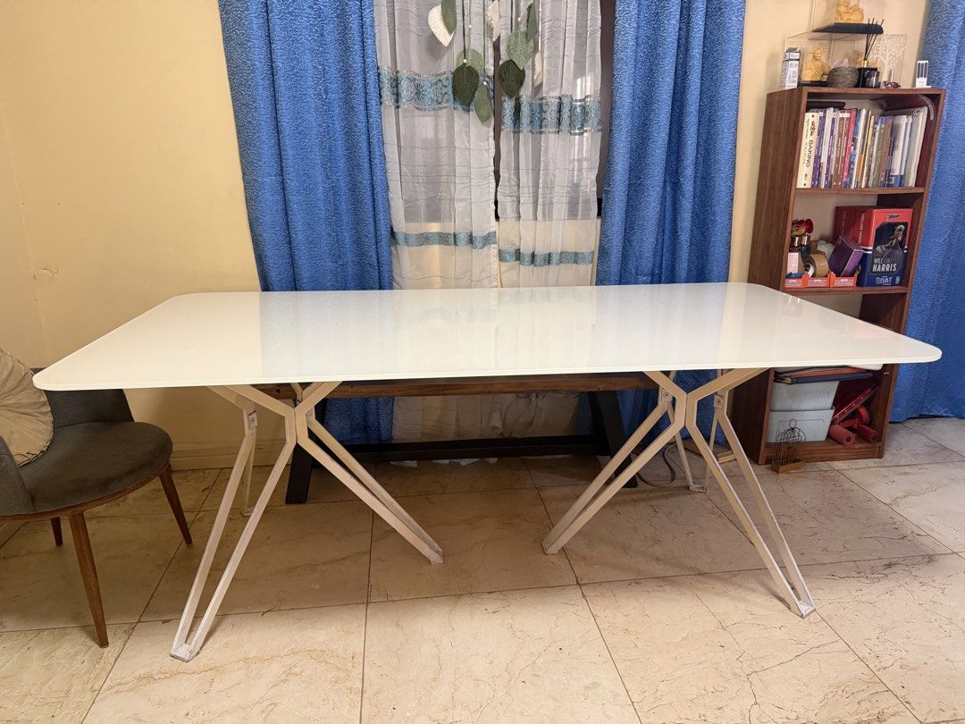 White Glass Top Dining Table with Unique Metal Legs (Category: Tables & Sets) located in Cainta. Submitted by jtc23 (Listing ID 1443660893, Image 2). Description: - Sleek modern dining table - Smooth white glass top - Distinctive white metal base with criss-cross legs - Spacious design, ideal for dining rooms or as a large desk - Easy to clean surface - Perfect for gatherings and work sessions.