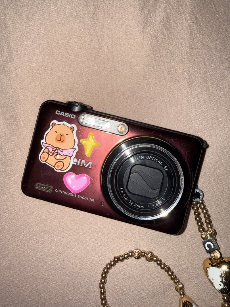 Casio EXILIM Digital Camera with Charm Strap (Category: Cameras) located in Las Pinas. Submitted by coolthreadz (Listing ID 1443880874, Image 1). Description: - Cute maroon Casio EXILIM digital camera - 5x optical zoom - Comes with a beaded charm strap with heart details - Features stickers on the front - Screen has minor scratches - Perfect for capturing memories.