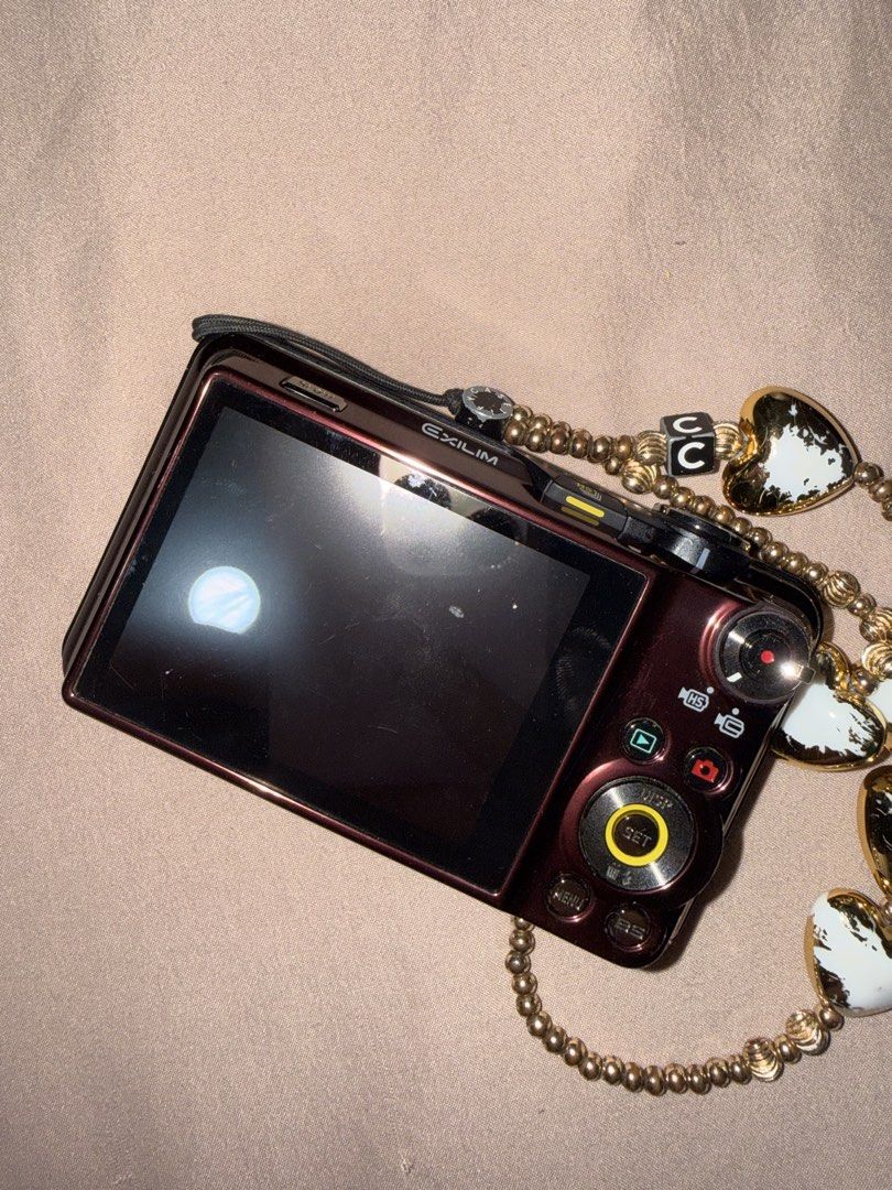 Casio EXILIM Digital Camera with Charm Strap (Category: Cameras) located in Las Pinas. Submitted by coolthreadz (Listing ID 1443880874, Image 3). Description: - Cute maroon Casio EXILIM digital camera - 5x optical zoom - Comes with a beaded charm strap with heart details - Features stickers on the front - Screen has minor scratches - Perfect for capturing memories.