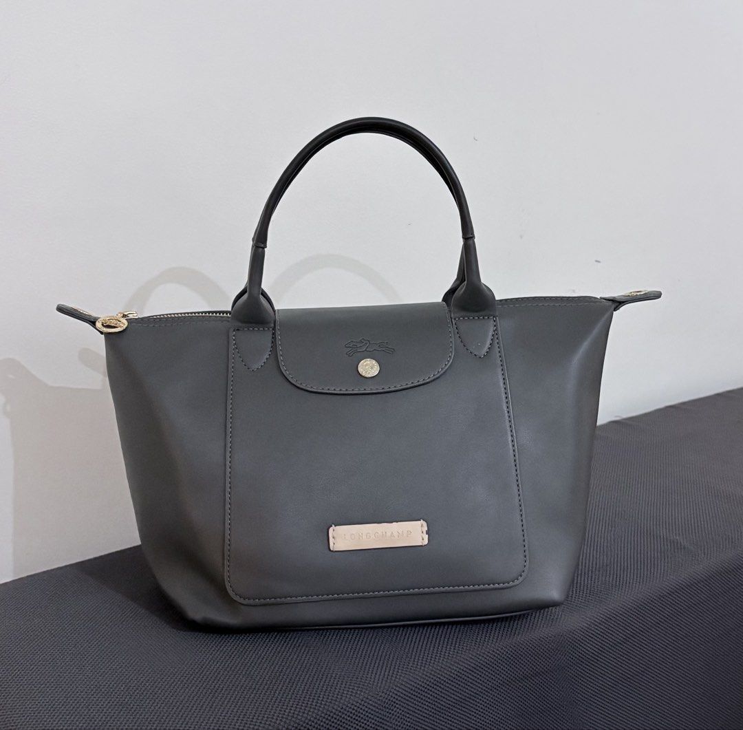 Longchamp Le Pliage Cuir Top Handle Bag (Category: Luxury Bags & Wallets) located in Manila. Submitted by klonlines03584 (Listing ID 1443871046, Image 1). Description: - Dark grey Longchamp handbag - Genuine leather material - Front pocket with snap closure - Top zipper closure - Two top handles.