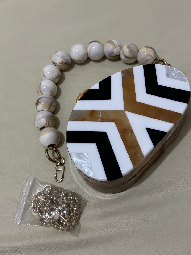 Elegancia 2-way Clutch Bag (Category: Clutches) located in Makati City. Submitted by aamii29 (Listing ID 1443970009, Image 3). Description: - Unique oval acrylic clutch - Eye-catching geometric pattern in brown, black, and white - Comes with a detachable beaded handle - Includes a versatile gold chain strap - Ideal for parties, events, or special occasions - Bought for ₱1,500. Selling for ₱800 - RFS: Decluttering.