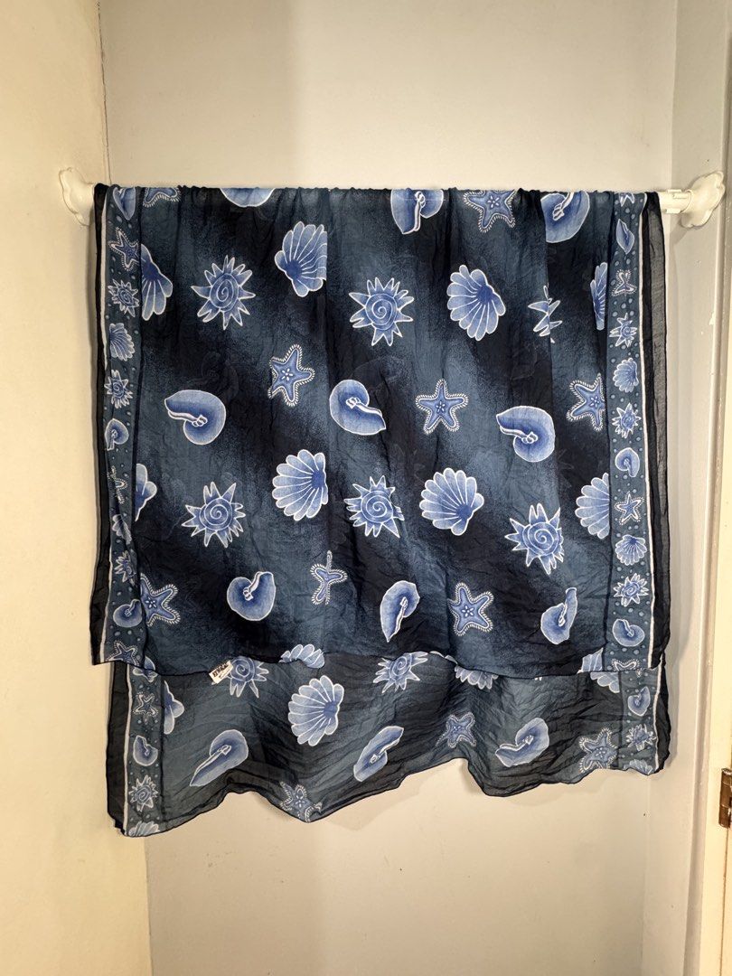 Navy blue shawl/Sea shell print cover up (Category: Scarves) located in San Juan City. Submitted by matchlessgetup.ph (Listing ID 1444015797, Image 3). Description: The fabric is adorned with various ocean-inspired motifs, including scalloped sea shells, spiral nautilus shells, starfish, and stylized sun-like or sea urchin symbols. This type of shawl is commonly used as a fashion accessory or a beach pareo due to its flowy drape and coastal aesth
