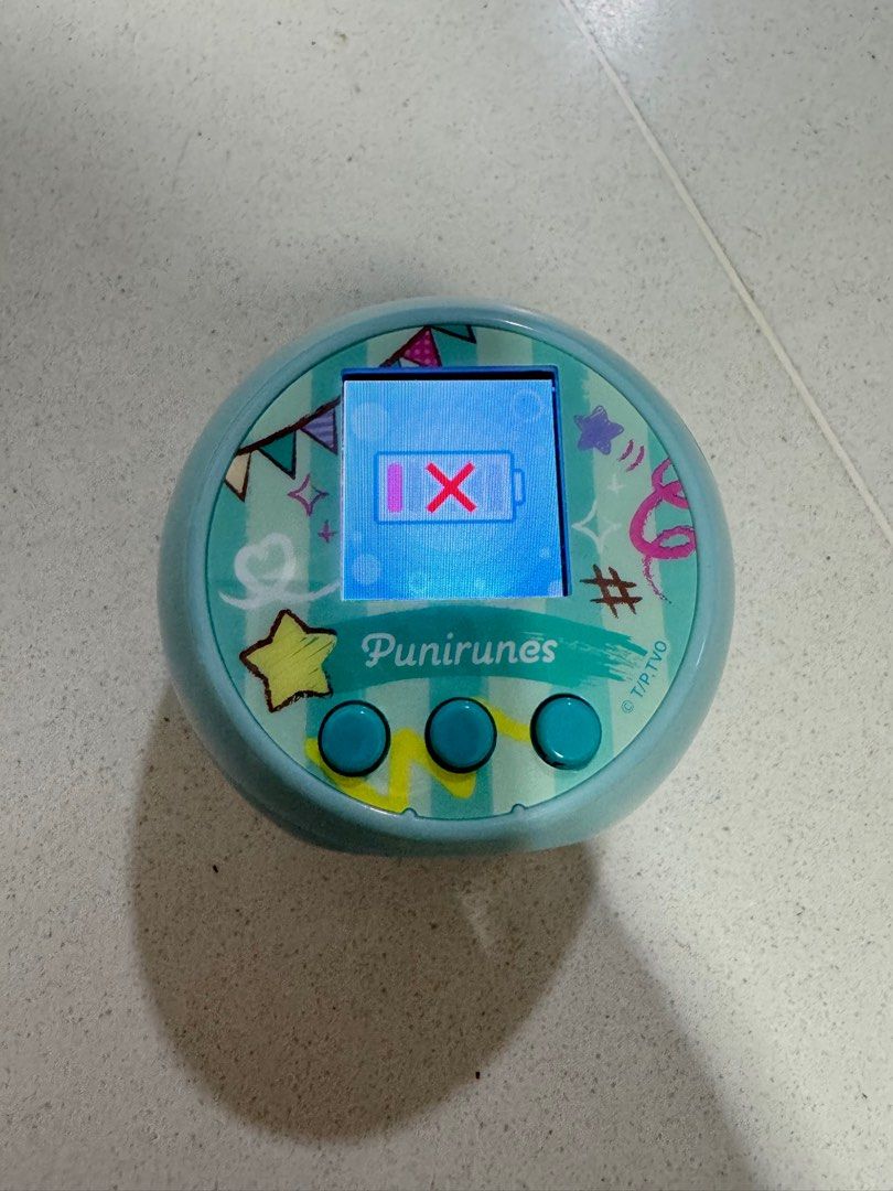 Tomy PuniRunes Virtual Pet Tamagotchi Style Toy (Category: Interactive Toys) located in Singapore. Submitted by pigshi (Listing ID 1443921110, Image 1). Description: - Light blue PuniRunes virtual pet toy - Made by Tomy - Screen displays a low battery icon with an X - Requires batteries (not included) - Fun handheld electronic game.