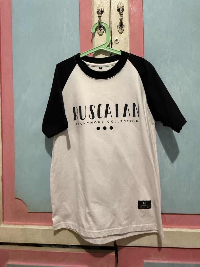 Buscalan Anonymous Collection Raglan T-shirt (Category: Tshirts & Polo Shirts ) located in Manila. Submitted by prelovedbyshai_116 (Listing ID 1444226245, Image 1). Description: - White and black raglan t-shirt from Buscalan Anonymous Collection. - Front features 'BUSCALAN' and 'ANONYMOUS COLLECTION' text. - Back graphic depicts 'the last mambabatol' with an elder figure. - Tagged 'AC'. - Perfect for casual everyday wear. -Used once -bought in Bu