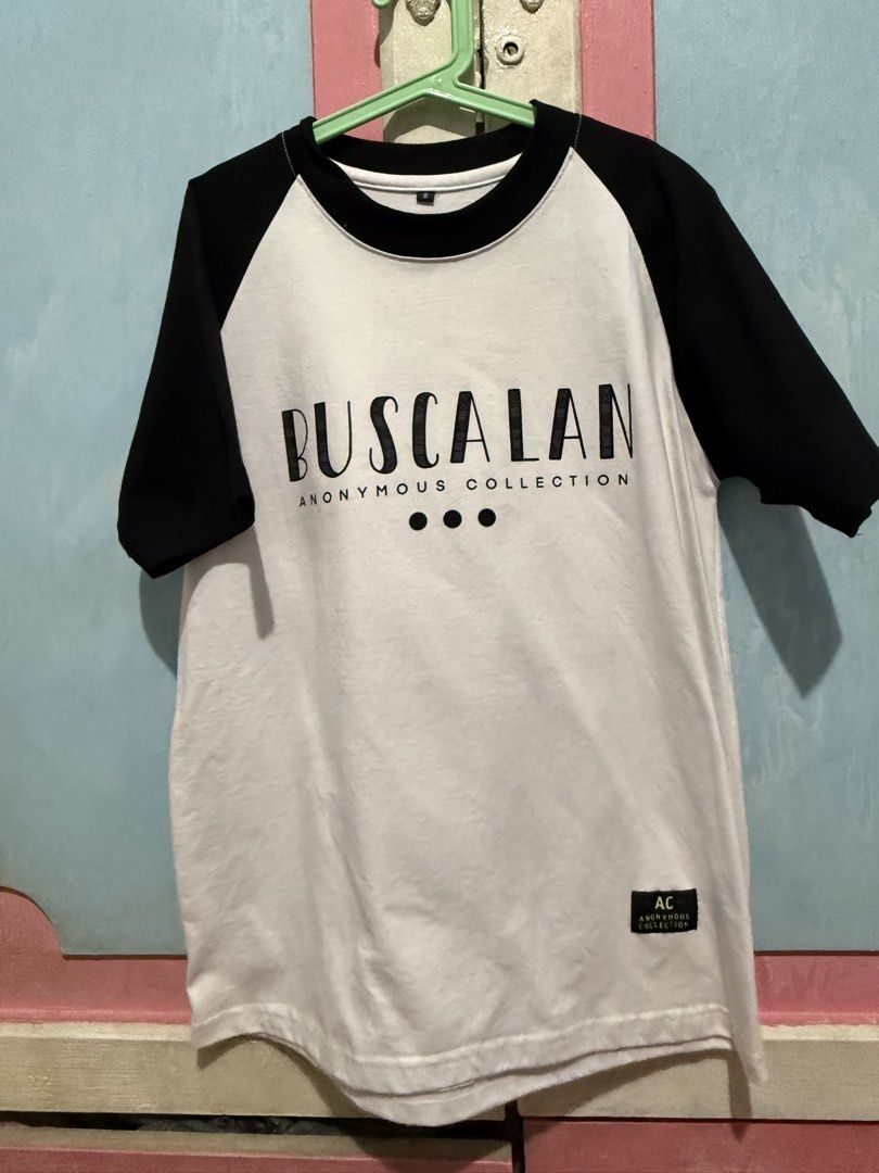 Buscalan Anonymous Collection Raglan T-shirt (Category: Tshirts & Polo Shirts ) located in Manila. Submitted by prelovedbyshai_116 (Listing ID 1444226245, Image 2). Description: - White and black raglan t-shirt from Buscalan Anonymous Collection. - Front features 'BUSCALAN' and 'ANONYMOUS COLLECTION' text. - Back graphic depicts 'the last mambabatol' with an elder figure. - Tagged 'AC'. - Perfect for casual everyday wear. -Used once -bought in Bu