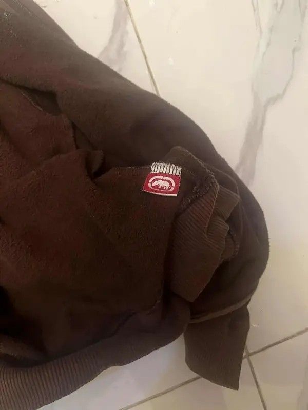 Ecko Unltd. Brown Zip-Up Hoodie (Category: Hoodies) located in Manila. Submitted by ixgri (Listing ID 1444260983, Image 3). Description: - Brand: Ecko Unltd. - Color: Brown - Style: Zip-up hoodie - Size: L - Features: Large graphic print on front with rhinos and green lettering - Material: Cotton and polyester blend - Best for: Casual wear.