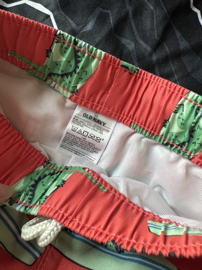 Under Armour Rash Guard & Old Navy Swim Trunks Set (Category: Babies & Kids Fashion) located in Quezon City. Submitted by amcadona (Listing ID 1444298281, Image 2). Description: - Under Armour rash guard: Black and white lightning pattern with red logo. - Old Navy swim trunks: Red base with green alligator and surfboard print. - Swim trunks feature an elastic waistband with a drawstring for a secure fit. - Ideal for beach days, pool parties, or a