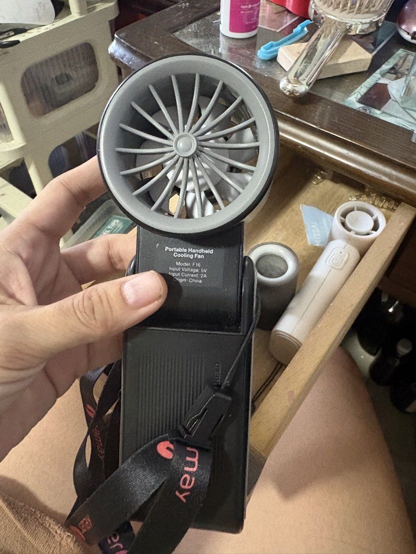 Jamay Portable Handheld Cooling Fan with Lanyard (Category: Fans) located in Manila. Submitted by crisdancal (Listing ID 1444355654, Image 2). Description: - Portable handheld cooling fan - Color: Black with grey accents - Includes attached lanyard - Input Voltage: 5V - Input Current: 2A - Compact and easy to carry for cooling on the go.