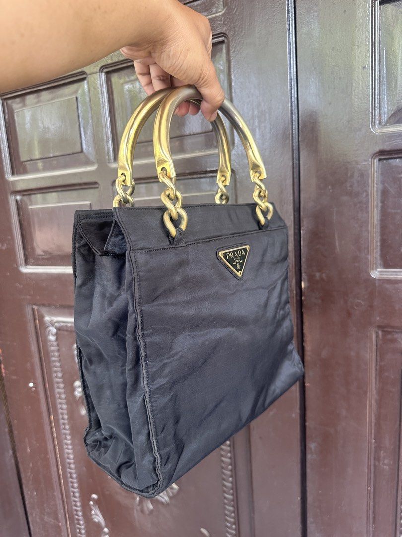 Prada Nylon Handbag with Gold Chain Handles (Category: Luxury Bags & Wallets) located in Bustos. Submitted by theprelovedshopbulacan (Listing ID 1444312631, Image 2). Description: - Authentic Black Prada Nylon Handbag - Elegant Gold Chain and Metal Handles - Signature Prada Triangle Logo on Front - Spacious Interior for Essentials - Perfect for Daily Use or Special Occasions - A Timeless Prada Accessory.