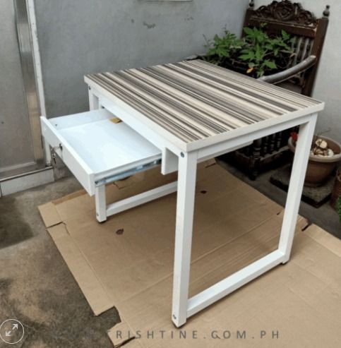 Stylish Mini Study Table (Category: Tables & Sets) located in Caloocan City. Submitted by jimtapitan_trishtinecorp. (Listing ID 1444373120, Image 2). Description: - Chic desk with a white metal frame - Unique brown and beige striped tabletop - Convenient pull-out drawer for storage - Ideal for compact workspaces or study nooks - Simple assembly and lightweight for easy relocation DISCLAIMER: PRICE IS FOR POSTING PURPOSES ONLY.