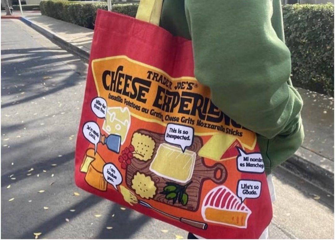 Trader Joe's Cheese Experience Red Tote Bag (Category: Tote Bags) located in San Juan City. Submitted by ipoundless (Listing ID 1444583321, Image 2). Description: - Cute red tote bag from Trader Joe's - Features a fun cheese theme with various cheese types and sayings - "Turophile" printed on the bottom (meaning cheese lover) - Bright yellow handles - Ideal for grocery shopping or everyday use - Showcases the Trader Joe's logo.