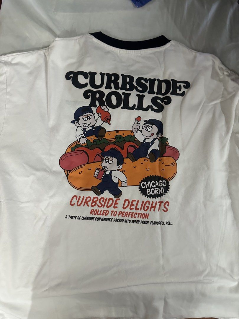 WEGO Curbside Rolls Graphic T-shirt (Category: Tshirts & Polo Shirts ) located in Dasmarinas. Submitted by kyle_47 (Listing ID 1444502096, Image 2). Description: - White graphic tee from WEGO - Black collar trim - Small 'CURBSIDE ROLLS' logo on front - Large graphic on back with cartoon characters, hot dog, and text ('CURBSIDE ROLLS', 'CHICAGO BORN!', 'CURBSIDE DELIGHTS', 'ROLLED TO PERFECTION') - Fun streetwear style.