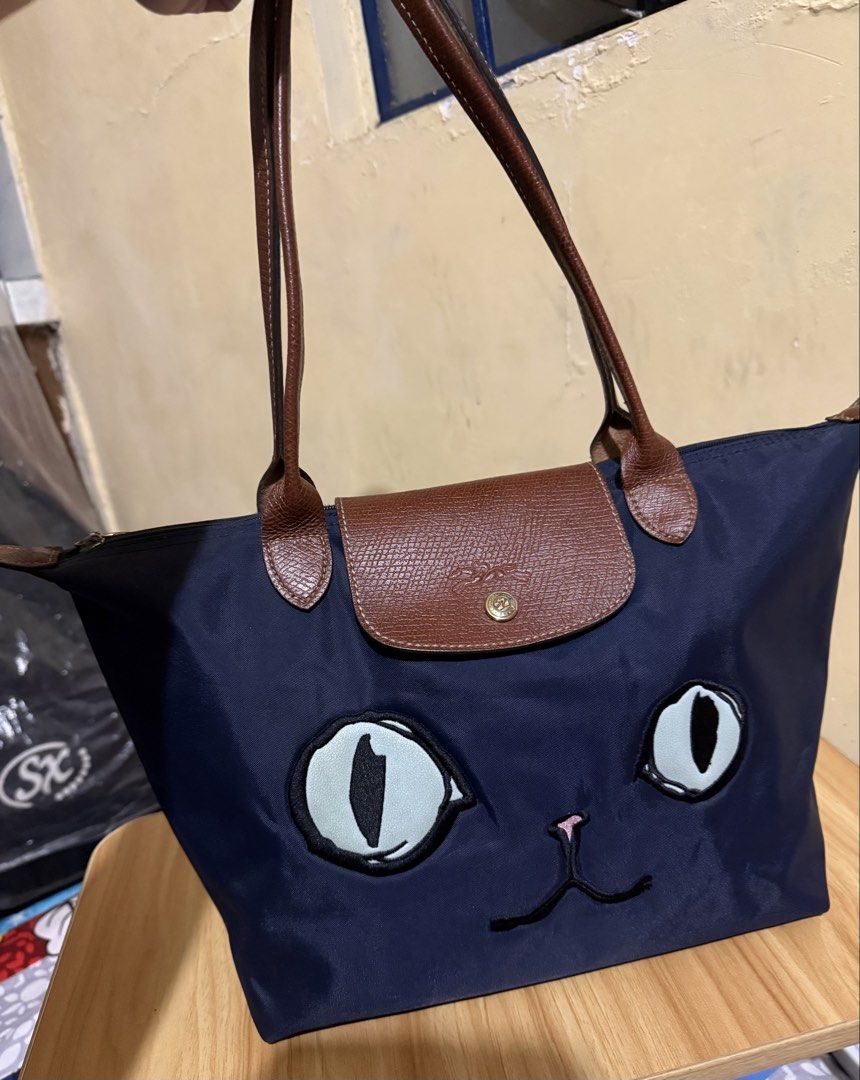 Longchamp Le Pliage Limited Edition Miaou (Category: Luxury Bags & Wallets) located in Caloocan City. Submitted by chnnnnns (Listing ID 1444827903, Image 1). Description: - Adorable navy blue tote bag - Features a cute cat face design on the front - Durable brown leather handles - Secure flap and zipper closure for the main compartment - Fun 'MIAOW' detail on the back - Ideal for everyday use or as a stylish accessory.