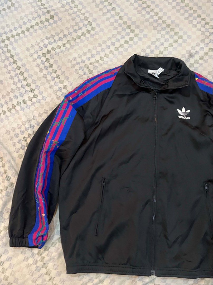 Adidas Track Jacket Black Blue Pink Stripes (Category: Coats, Jackets and Outerwear) located in Batangas. Submitted by gavsandrix (Listing ID 1441462080, Image 2). Description: - Classic Adidas track jacket - Black base with iconic three stripes on sleeves - Stripes feature blue and pink with a paint splatter effect - Full zip front closure - Convenient pockets - Perfect for casual wear or sports activities.