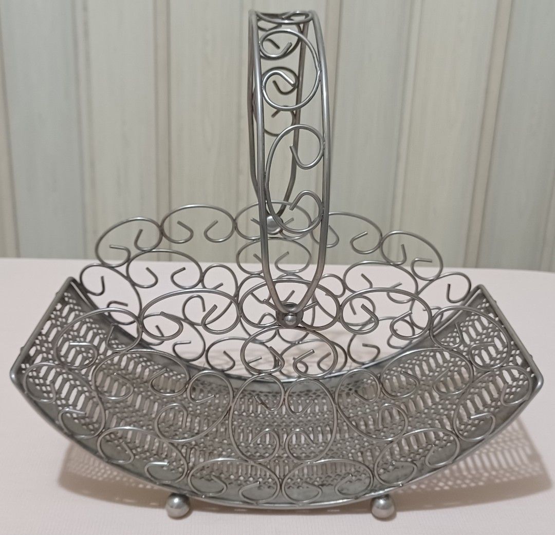 Decorative Metal Wire Basket with Handle (Category: Storage Boxes & Baskets) located in Quezon City. Submitted by wjmae (Listing ID 1441427182, Image 2). Description: - Decorative metal wire basket - Features an ornate handle - Intricate scrollwork along the sides - Woven pattern on the base - Stands on small ball feet - Ideal for holding fruit, flowers, or general organization - Adds a vintage aesthetic to any room.