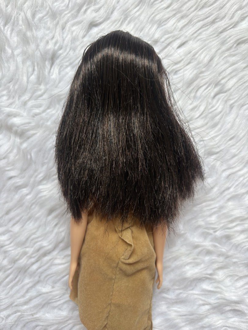 Preloved Barbie Doll (Category: Kids Toys) located in Bulacan. Submitted by lmsdeclutteringcorner (Listing ID 1441422476, Image 3). Description: - Barbie doll with long, dark hair. - Features a tan, one-shoulder fringed dress. - Dress has a colorful embroidered neckline. - Doll is displayed on a fluffy white rug. - Ideal for collectors and playtime..