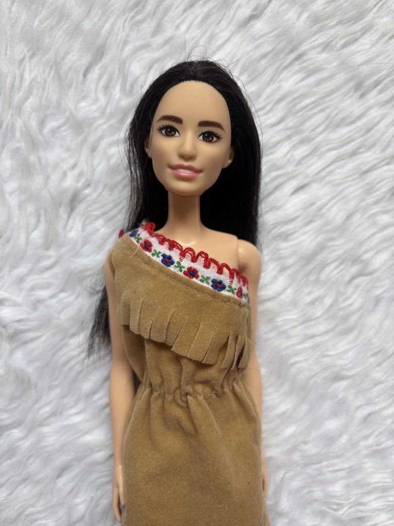Preloved Barbie Doll (Category: Kids Toys) located in Bulacan. Submitted by lmsdeclutteringcorner (Listing ID 1441422476, Image 2). Description: - Barbie doll with long, dark hair. - Features a tan, one-shoulder fringed dress. - Dress has a colorful embroidered neckline. - Doll is displayed on a fluffy white rug. - Ideal for collectors and playtime..